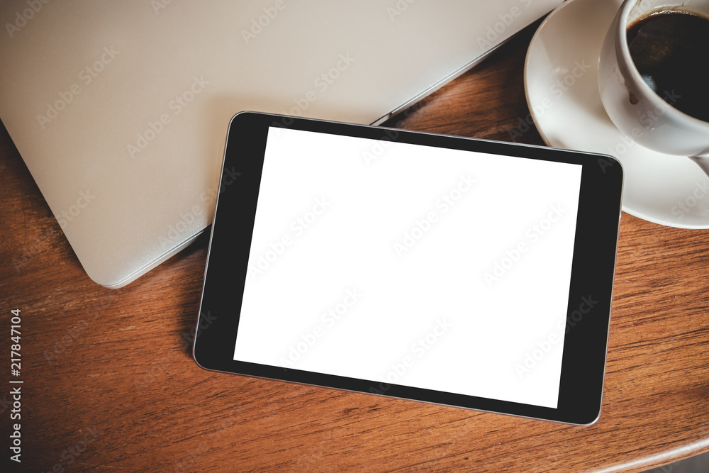 Top view mockup image of a black tablet pc with blank desktop white screen with laptop and coffee cup on wooden table Top view mockup image of a black tablet pc with blank desktop white screen with laptop and coffee cup on wooden table