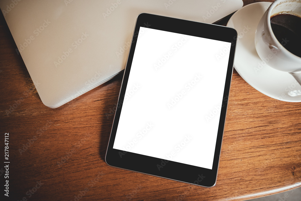 Top view mockup image of a black tablet pc with blank desktop white screen with laptop and coffee cup on wooden table Top view mockup image of a black tablet pc with blank desktop white screen with laptop and coffee cup on wooden table