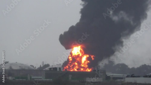 Huge fire blaze from burning oil container in refinery. Firefighter water jet extinguish the fire started near a petrol storage tank. Black rain, acid rain, smog, smoke, ash, ecological pollution
