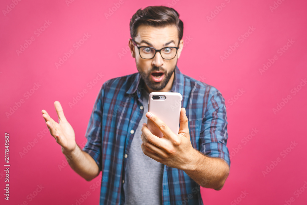 © denis_vermenko - Portrait of a surprised casual man looking at mobile phone isolated over pink background. © denis_vermenko - Portrait of a surprised casual man looking at mobile phone isolated over pink background.