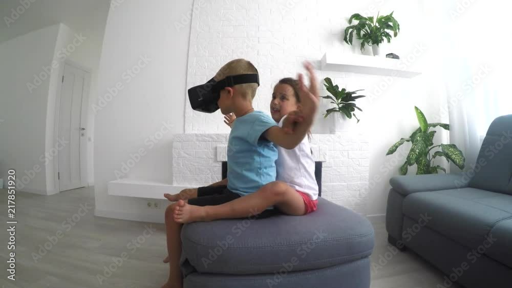 Amazed kids using virtual reality headsets and pointing up with finger while sitting Amazed kids using virtual reality headsets and pointing up with finger while sitting