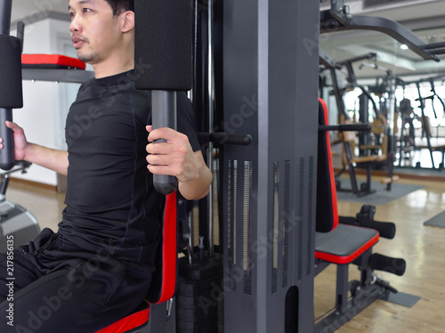 Fit young Asian man exercising with machine at sport gym. Fitness and workout concept