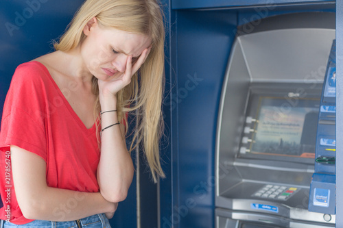 Sad woman standing in front of a ATM bank machine. No money.