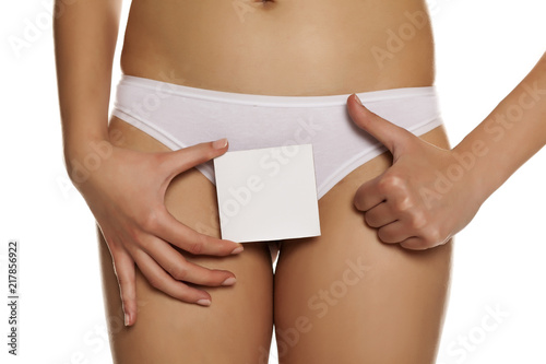 Woman in panties cowers her vagina with empty sheet of paper on white background and showing thumbs up