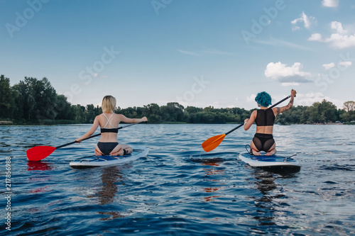 back view of sportive girls surfing on paddle boards on river