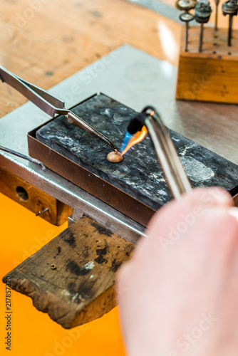 Soldering with a torch flame a jewelry piece at workshop of goldsmith