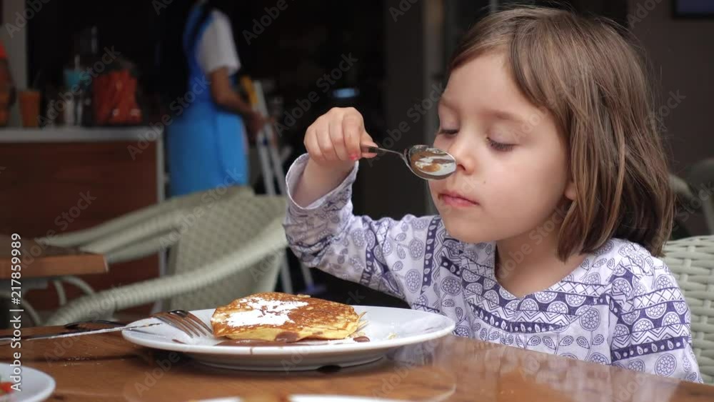 Girl eats pancakes, poured with chocolate and sprinkled with powdered sugar. Girl eats pancakes, poured with chocolate and sprinkled with powdered sugar.