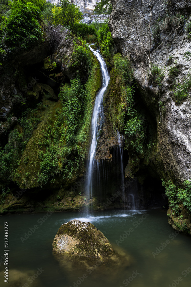 Cascada que cae sobre un río con una roca en el Nacedero del Urederra Cascada que cae sobre un río con una roca en el Nacedero del Urederra