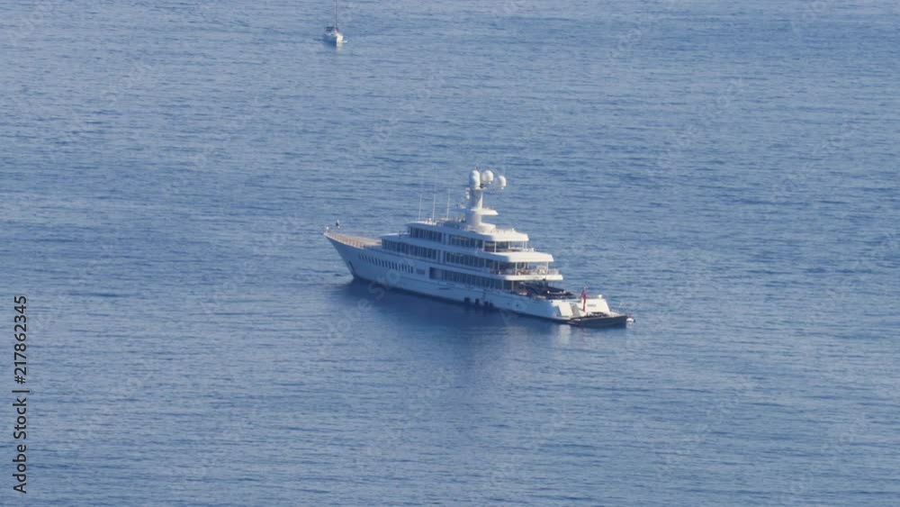 Close up view to a beautiful yacht drifting on the surface of peaceful blue sea. Another small boat slowly approaching on the background.