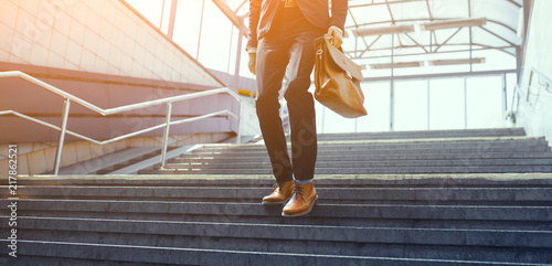 Man in suit walking down stairs. Formaly dressed guy making his way down concrete staircase with brown leather bag in his hand. photo