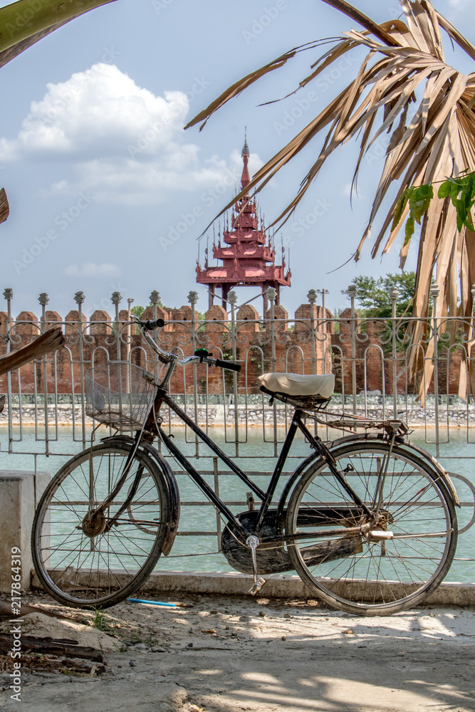 An old bicycle is lean on a railing over a water moat before the Royal Palace in Mandalay, Myanmar.