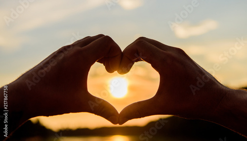 Heart gesture in front of sunset above river water surface  defocused. Top places for romantic date. Sunset sunlight romantic atmosphere. Male hands in heart shape gesture symbol of love and romance