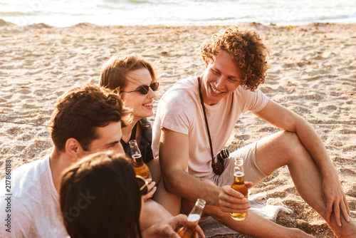 Group of friends outdoors on the beach sitting while drinking beer. © Drobot Dean