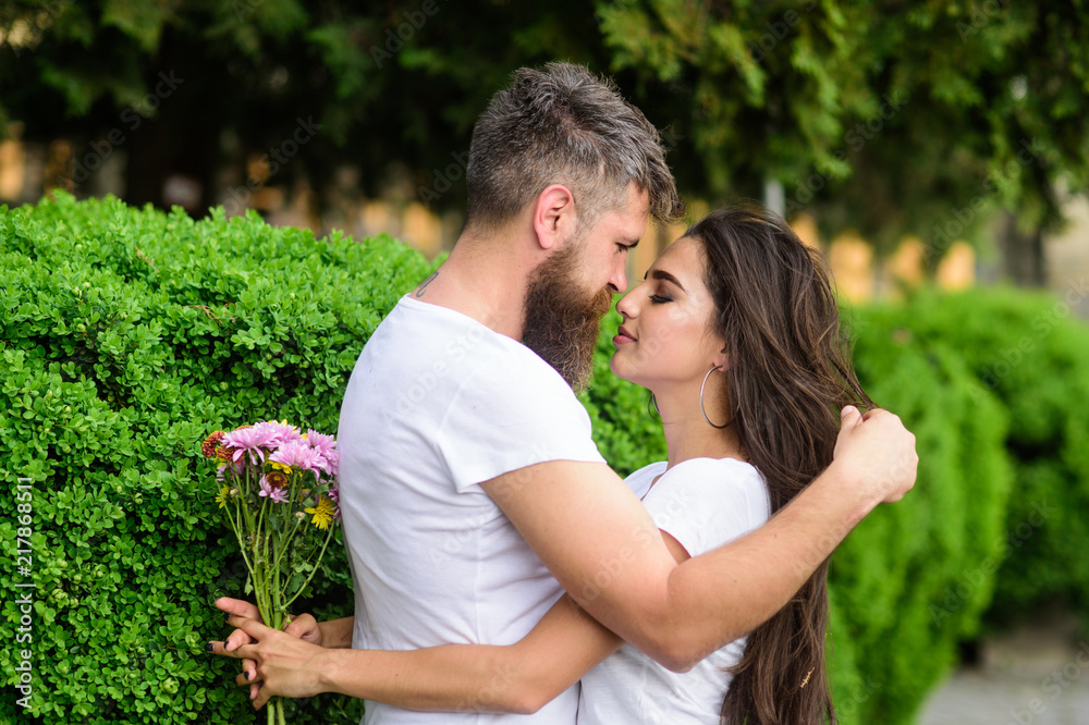 He likes her gorgeous hair. Girl holds flowers while man caress her long hair. Couple in love hugs outdoors park background. Man bearded hipster gently hugs girlfriend enjoying her soft long hair