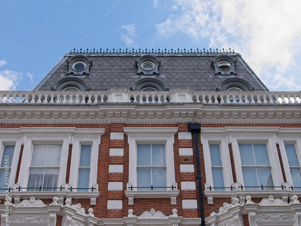 Obraz premium Details of Victorian townhouse exterior in London. Steep pitch terracotta tiled roof, cast iron railings, balustrade, sash windows and striped stonework.
