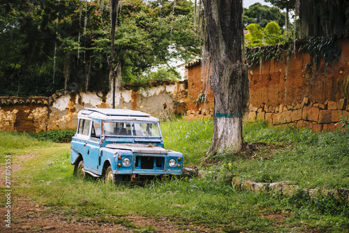 An old blue 4x4 stands under a gigantic tropical tree, Barichara/ Colombia/ South America