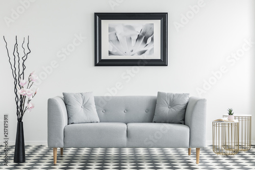 Flowers next to grey sofa with cushions in minimal living room interior with poster. Real photo
