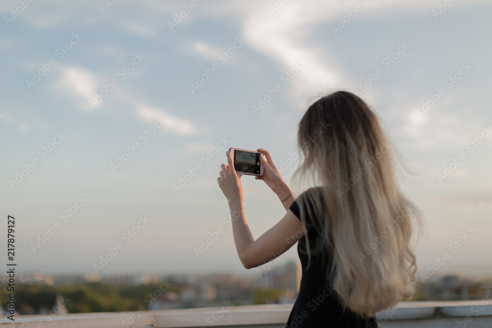Girl taking photos from the roof at sunset on smartphone Girl taking photos from the roof at sunset on smartphone