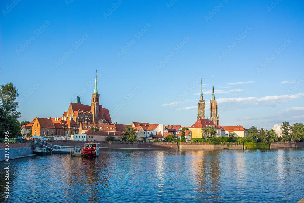 european old city street concept with many small red roof houses and two catholic cathedral church in river waterfront district and water surface reflection on foreground in summer bright day time