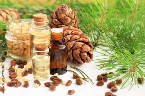 Set of bottles of essential oil of pine and  pinenut, fresh green branches, cones, and shelled cedar nuts. 