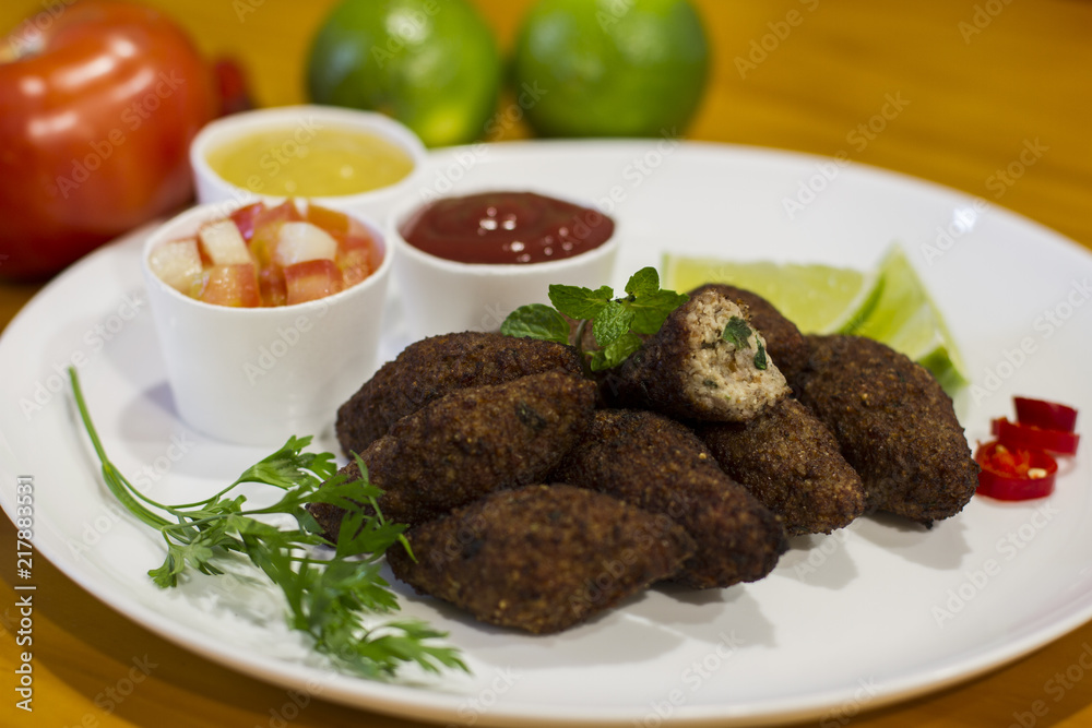 Traditional arabic food, kibes served on white plate accompanied by salad, ketchup, mustard and lemon on yellow wooden table Traditional arabic food, kibes served on white plate accompanied by salad, ketchup, mustard and lemon on yellow wooden table