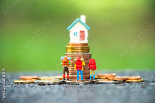 Miniature people, group of travelers standing on stack coins in front of mini house using as property and financial concept