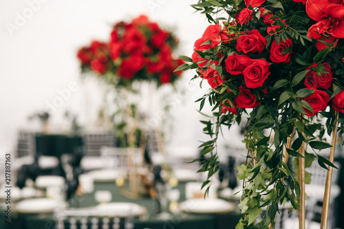 Tall bouquets of roses stand on dark green tables in restaurant hall