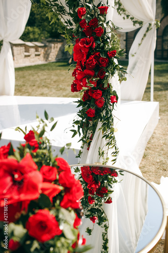 Red flowers and greenery decorate white wedding altar and little table before it