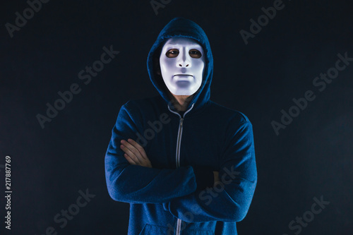 Fototapeta Naklejka Na Ścianę i Meble -  Anonymous masked man under hoodie with arms crossed isolated over dark background - incognito and mysterious criminal on internet activities concept.