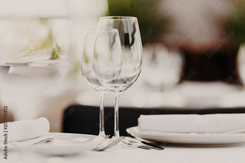 Wedding table set for banquet. Glasses and plates served on table. Dinner setting. Luxury cutlery. Festive event. Horizontal shot. Blurred background.