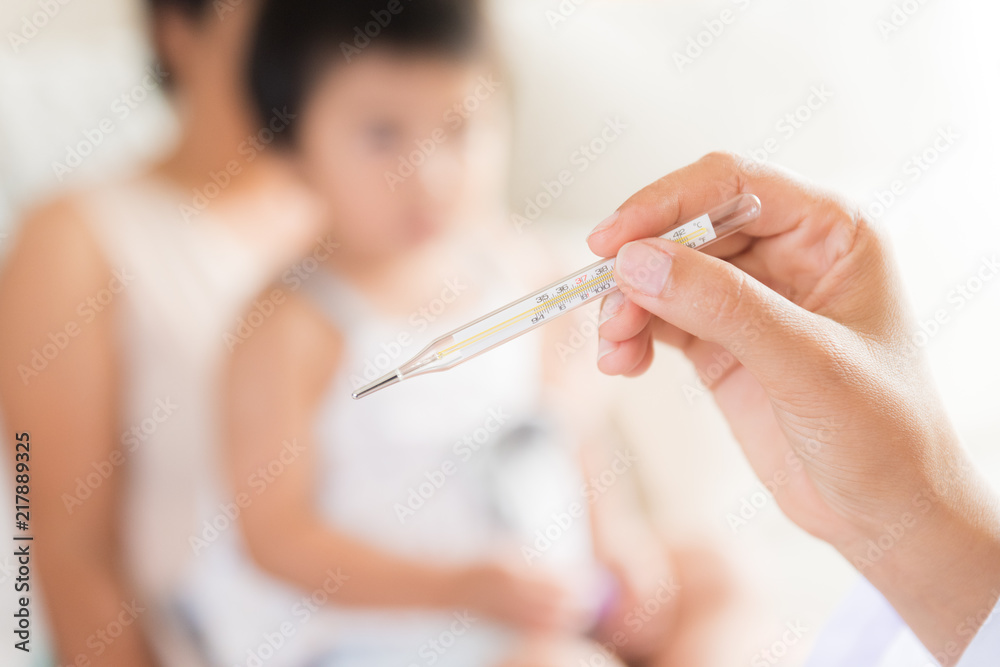 Doctor holding digital thermometer to measuring temperature of her ill kid and sick little girl with mother in background. Doctor holding digital thermometer to measuring temperature of her ill kid and sick little girl with mother in background.