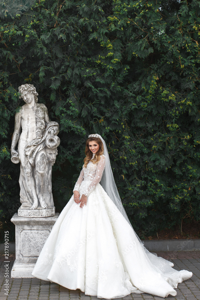 Charming bride poses before old antique statue in the garden