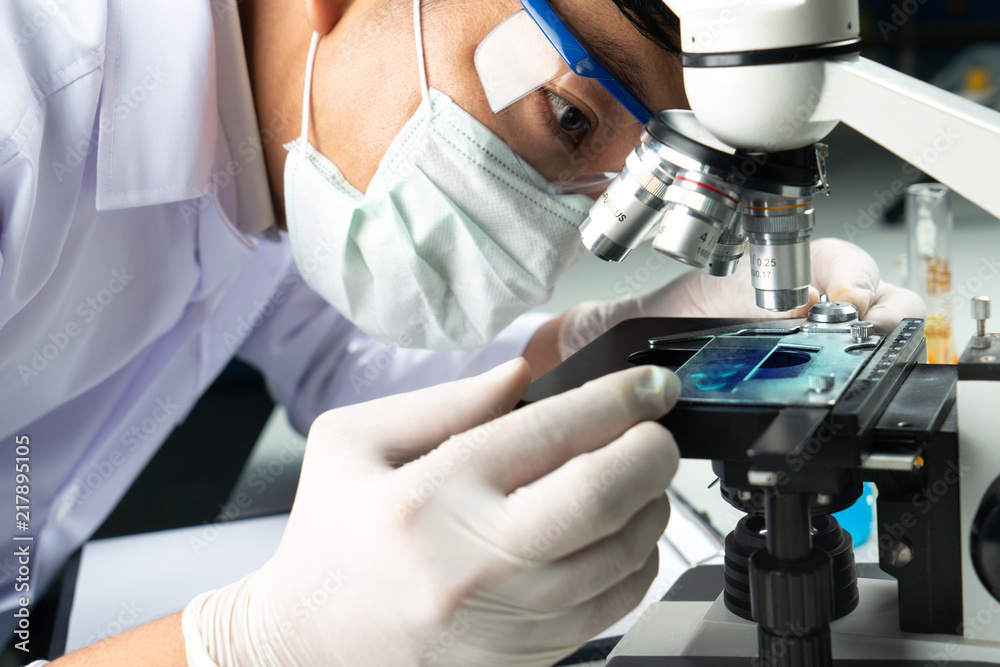 Hands of young Asian man and white microscope in science laboratory with blue liquid and dropper for testing. Technician dripping blue water on slide glass in science lab. Hands of young Asian man and white microscope in science laboratory with blue liquid and dropper for testing. Technician dripping blue water on slide glass in science lab.