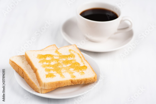Sliced bread with honey topping and cup of black coffee on white table, delicious breakfast