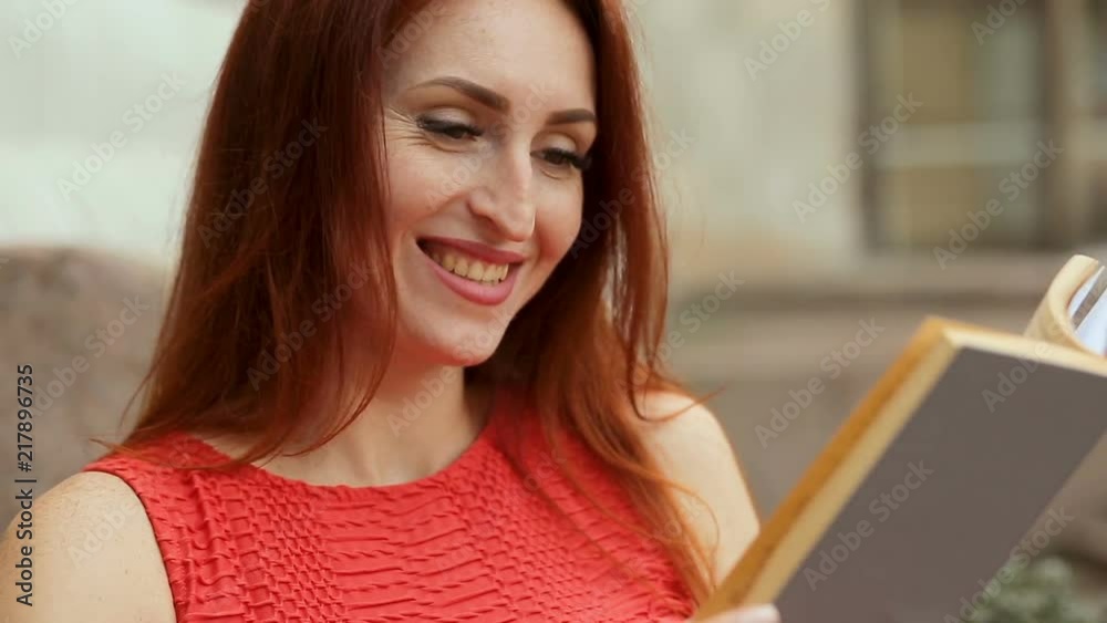 The smiling red haired woman reading book in park The smiling red haired woman reading book in park