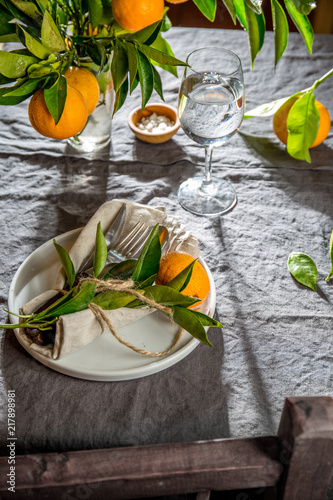 Table setting with white plate, cutlery, linen napkin and orange tree branch decoration on gray linen tablecloth . Close up. Table with table setting and shair