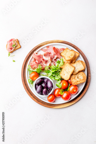 Antipasto Plate with dried bread, ham serrano, tomato cherry and purple olives. White background.