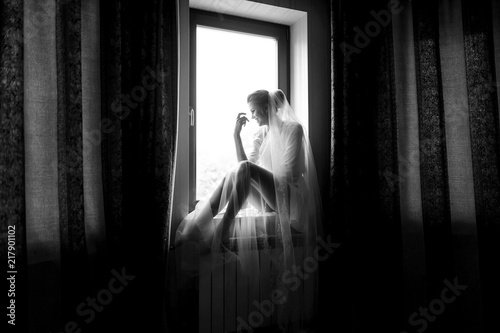 Laughing bride sits on the windowsill in the dark room
