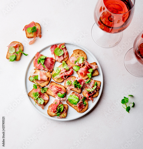Mini open sandwiches with jamon serrano on white plate and rose wine