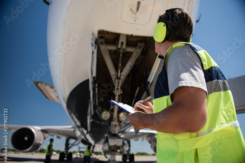 Detailed check. Low angle portrait of man in headphones writing on clipboard photo