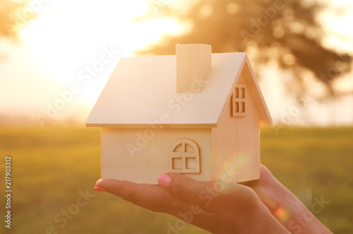 Image of woman holding small wooden house outdoors at sunset light.