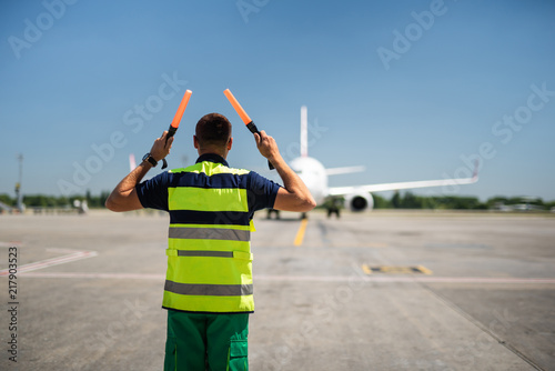 Directing the jet. Back view of aviation marshaller at airport. Aircraft, runway and sky on blurred background photo