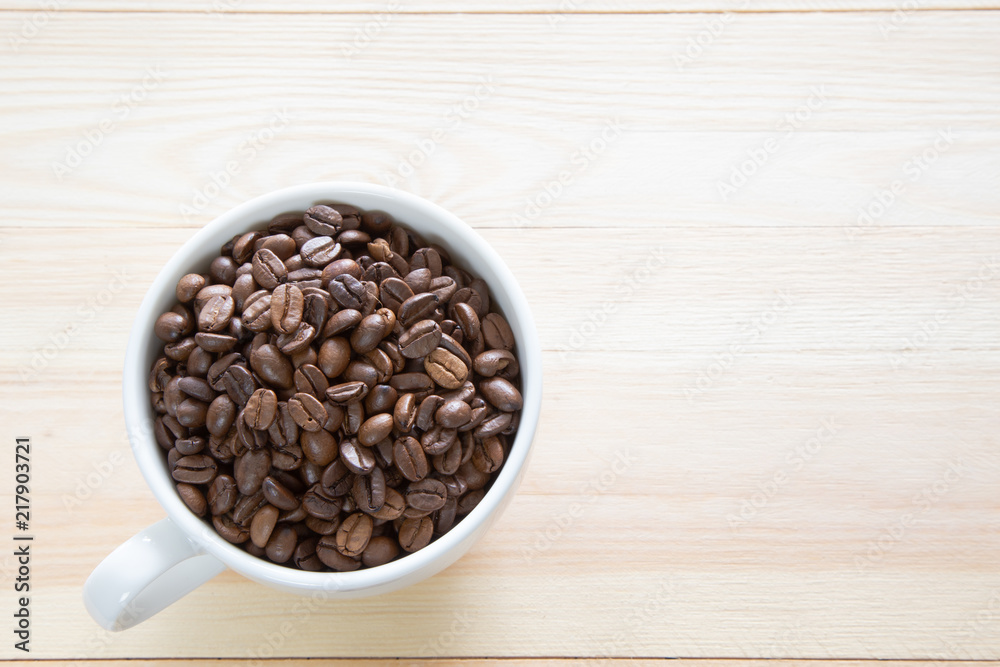 A coffee cup full with coffee beans on wooden background A coffee cup full with coffee beans on wooden background