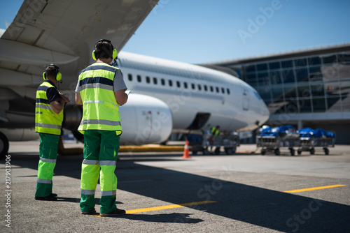 Waiting for the flight. Full length portrait of aviation crewmembers. Passenger airplane and trolleys with luggage on background