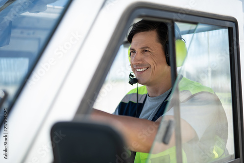 Happy driver. Side view of cheerful airport worker driving the car. He is wearing headphones with microphone