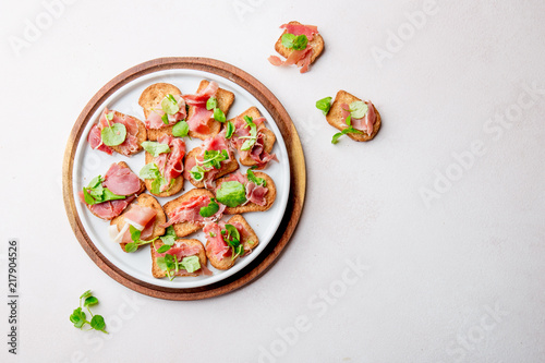 Mini open sandwiches with jamon serrano on white plate