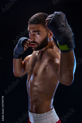 Boxing man ready to fight. Boxer with strong hands and clenched fists in blue straps against a black background © nazarovsergey