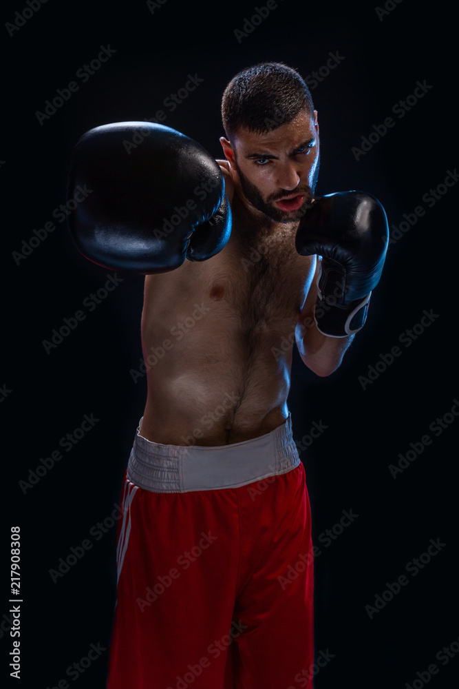The boxer is ready to deal a powerful blow. Photo of muscular man on black background.