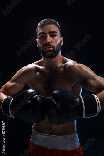 Young male boxer wearing his red boxing shorts and gloves on black background © nazarovsergey