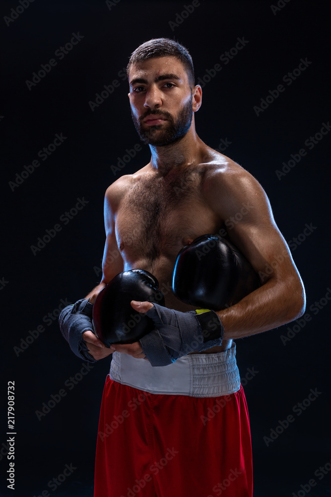 Handsome athletic guy in a red shorts on a black background. The boxer is fetching his breath after practicing hooks and blows.